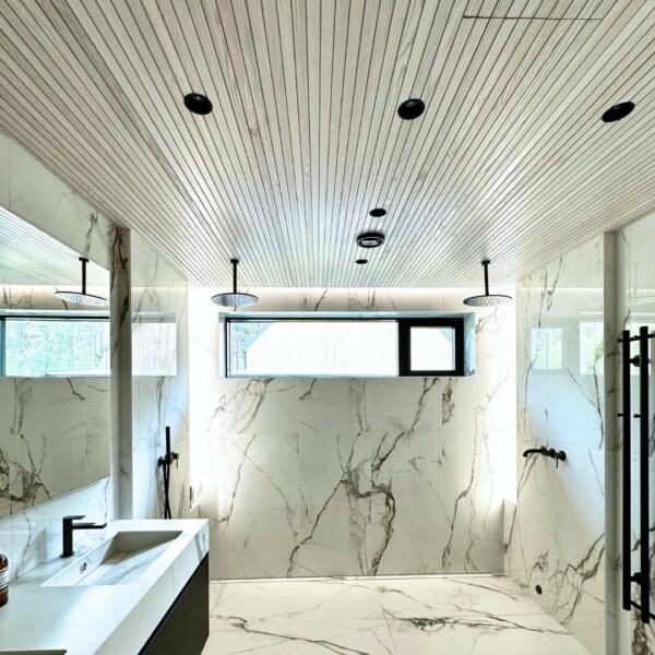 Entire bathroom with JALO interior panels on the ceiling, in a combination of marble and black details. The audible white surface of JALO panels creates light and harmony in the space, while the contrast of marble and black adds a modern elegance.