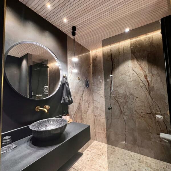 Bathroom with JALO decorative panels on the ceiling, combined with black and brown tones. The audible white surface of the panel beautifully reflects the light, highlighting the modern and warm contrast of the black and brown combination.