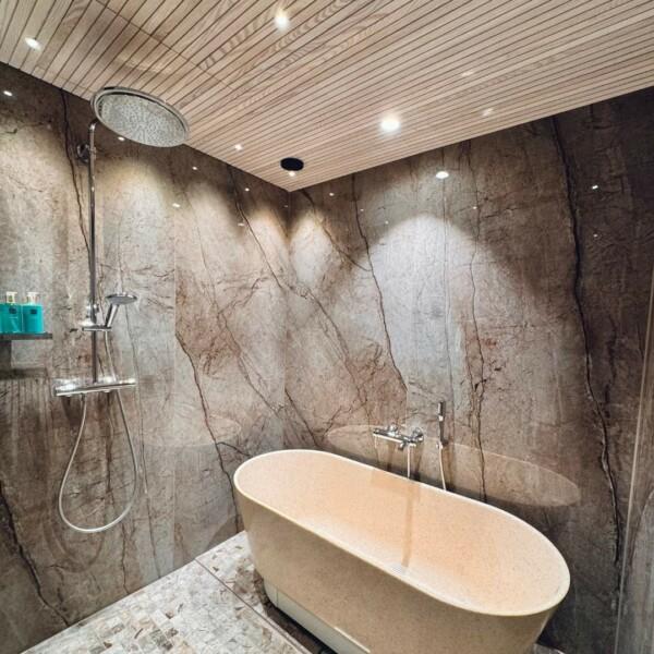 JALO interior panels on the bathroom ceiling combined with a modern bathtub and black and brown details. The audible white surface of the panel adds space and complements the soothing look of the bathtub.